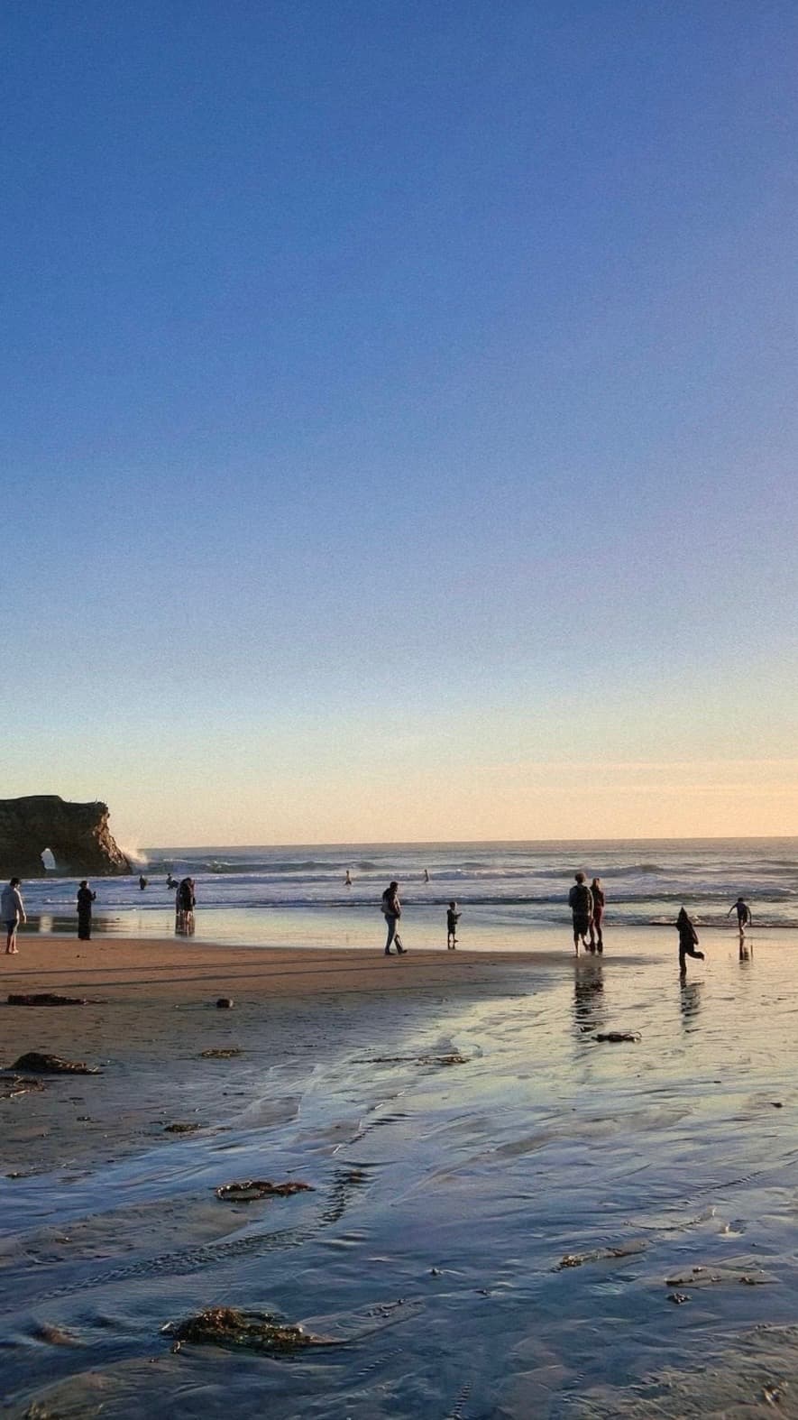 a beach at golden hour, people scattered along the shoreline